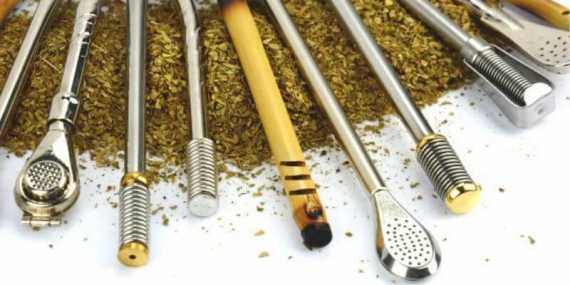 Diferentes tipos de bombillas para mate de acero inoxidable, alpaca y ca&ntilde;a, apoyadas sobre yerba mate.